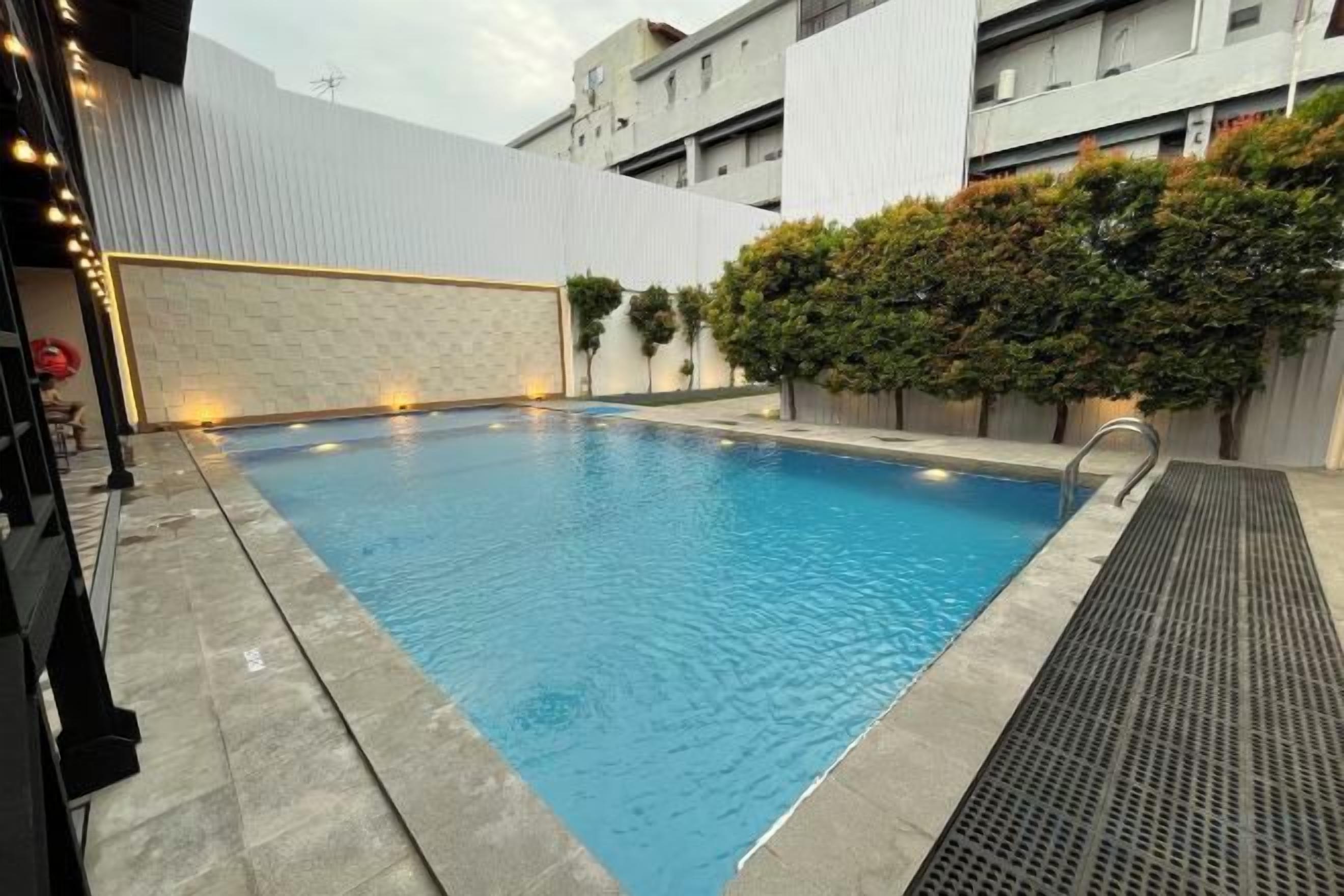 A rectangular swimming pool with a tiled edge, surrounded by a low wall and a hedge.