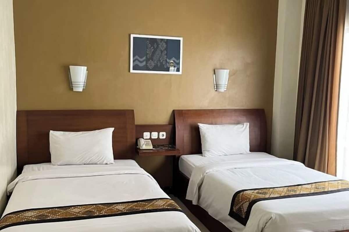 A hotel room with two beds, a nightstand with a phone, and a framed picture on the wall.