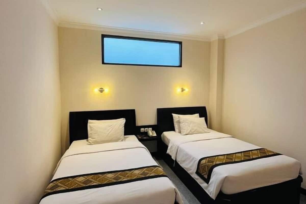 A hotel room with two single beds, a flat-screen TV mounted on the wall, and two wall-mounted reading lights.