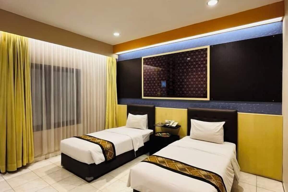 A hotel room with two beds, a large mirror, a nightstand, and a window with sheer curtains.