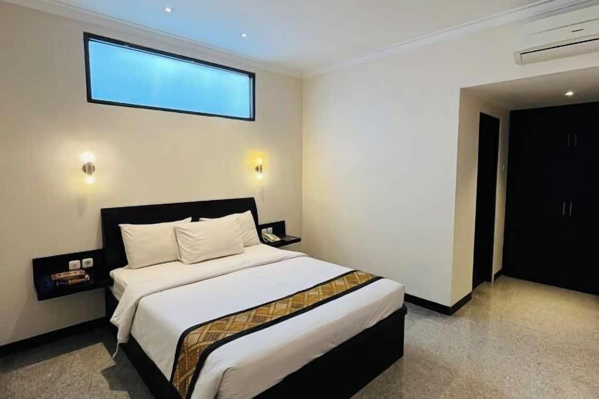 A hotel room with a large bed, bedside tables, a nightstand, a wall-mounted TV, and a door to the right.