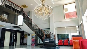 A spacious lobby with a grand chandelier, a staircase, and red seating areas. - Riez Palace Hotel (East Tegal)