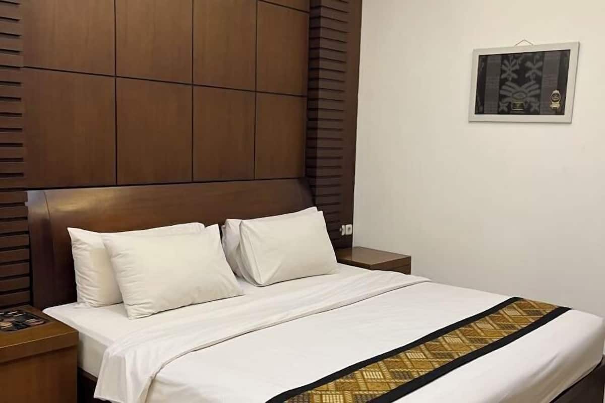 A hotel room with a wooden headboard, a bed with white bedding, a nightstand, and a framed picture on the wall.