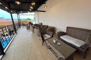 Un espacio de estar al aire libre cubierto con muebles de mimbre y una mesa, con vistas a un paisaje urbano.