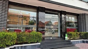 A hotel entrance with a glass facade, steps leading up to the door, and a reflection of the surrounding area. - Riez Palace Hotel (East Tegal)