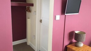 A hallway with a door, a mounted television, and a small table with a lamp. - The Kings Arms (London)