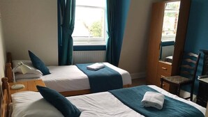 A hotel room with two single beds, a wooden chair, a desk, and a window with curtains. - The Kings Arms (London)