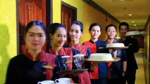 A group of hotel staff in uniform carrying trays with cups and a cake. - Grand Jambi (Jambi)