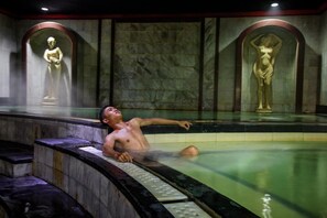 A man relaxing in a hot spring with statues in the background. - Grand Jambi (Jambi)