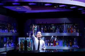 A bar area with shelves of liquor bottles and a bartender. - Grand Jambi (Jambi)