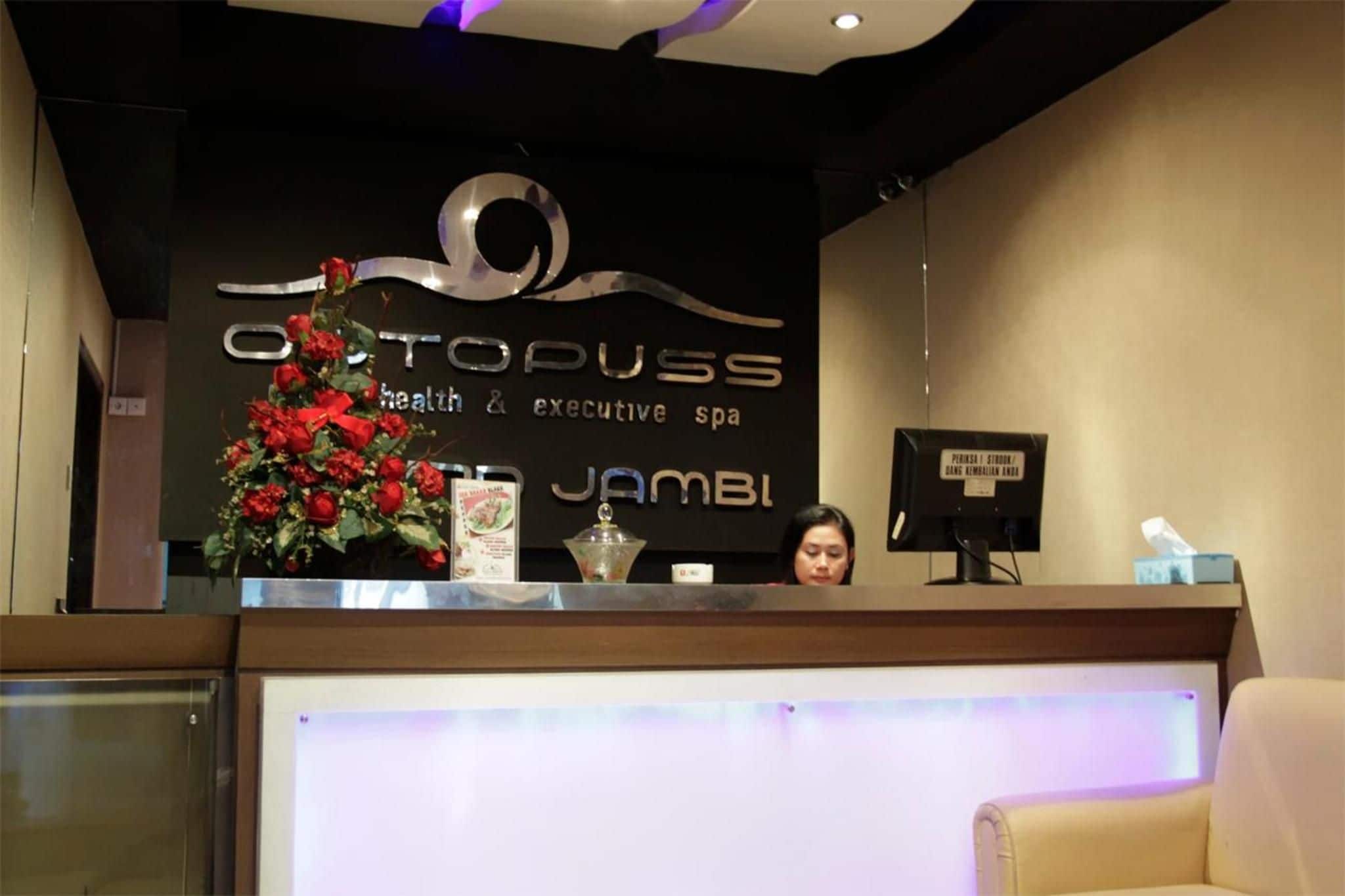 A reception desk with a sign for 'Optopuss Health & Executive Spa' and a decorative floral arrangement.