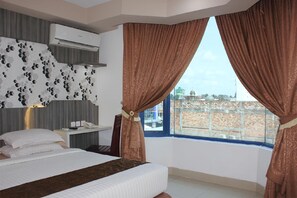 A hotel room with a bed, a desk with a phone, and a window with curtains. - Grand Jambi (Jambi)