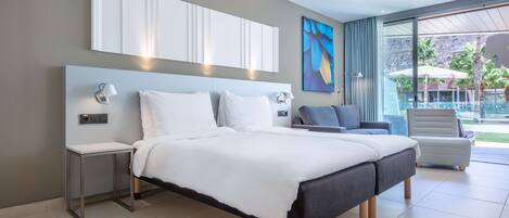 A modern hotel room with a large bed, a small table, a chair, and a view of a pool and greenery outside.