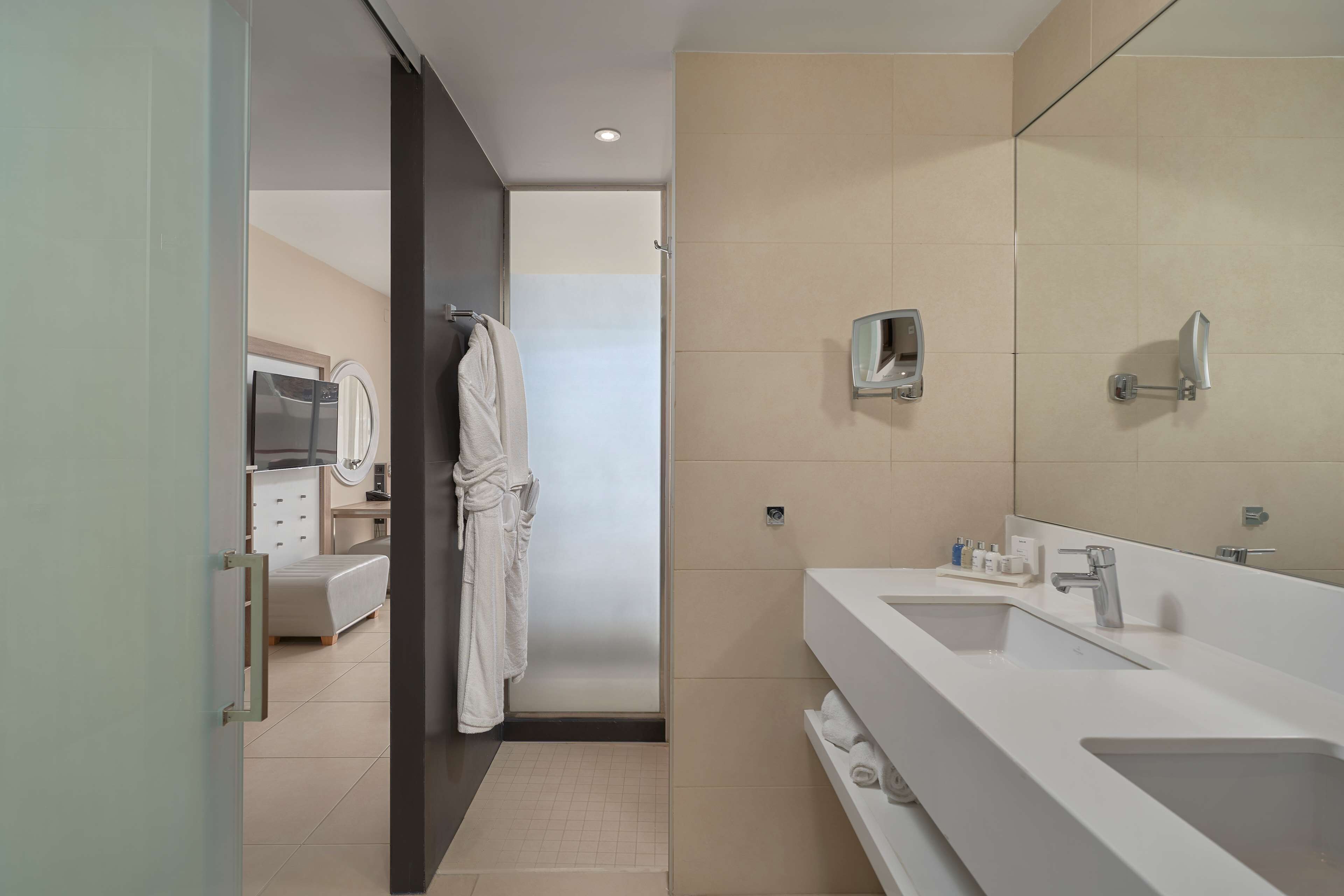 A modern bathroom with a large mirror, two sinks, and a robe hanging on a rack.