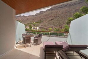 A balcony with wicker furniture, a table, and a view of a mountainous landscape.