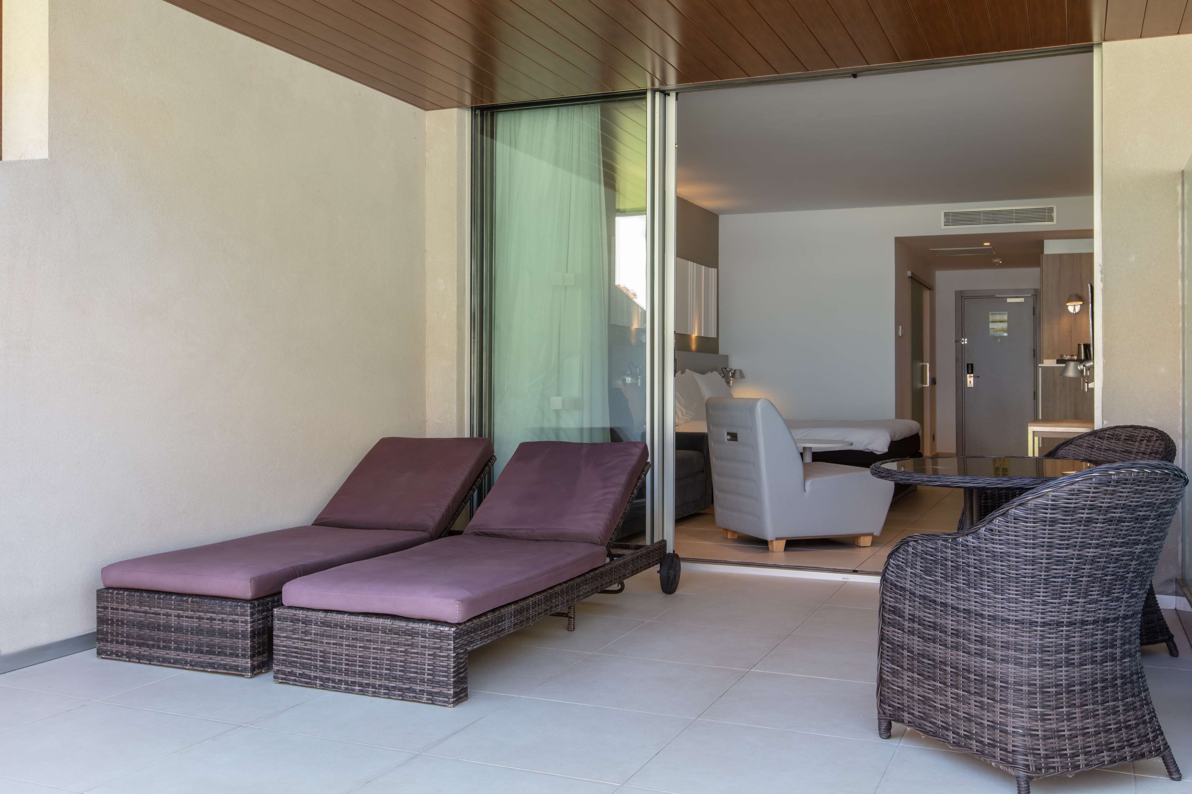 A modern outdoor lounge area with wicker furniture, a glass partition, and a view into the interior.