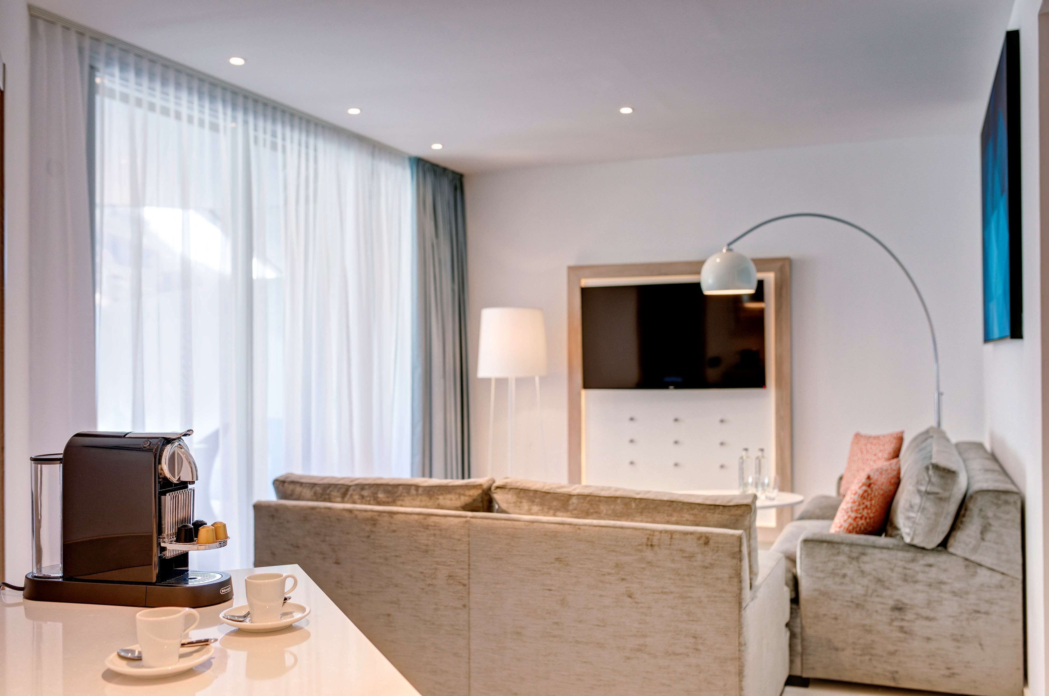Una habitación de hotel moderna con cafetera, sofá, televisor y lámpara.