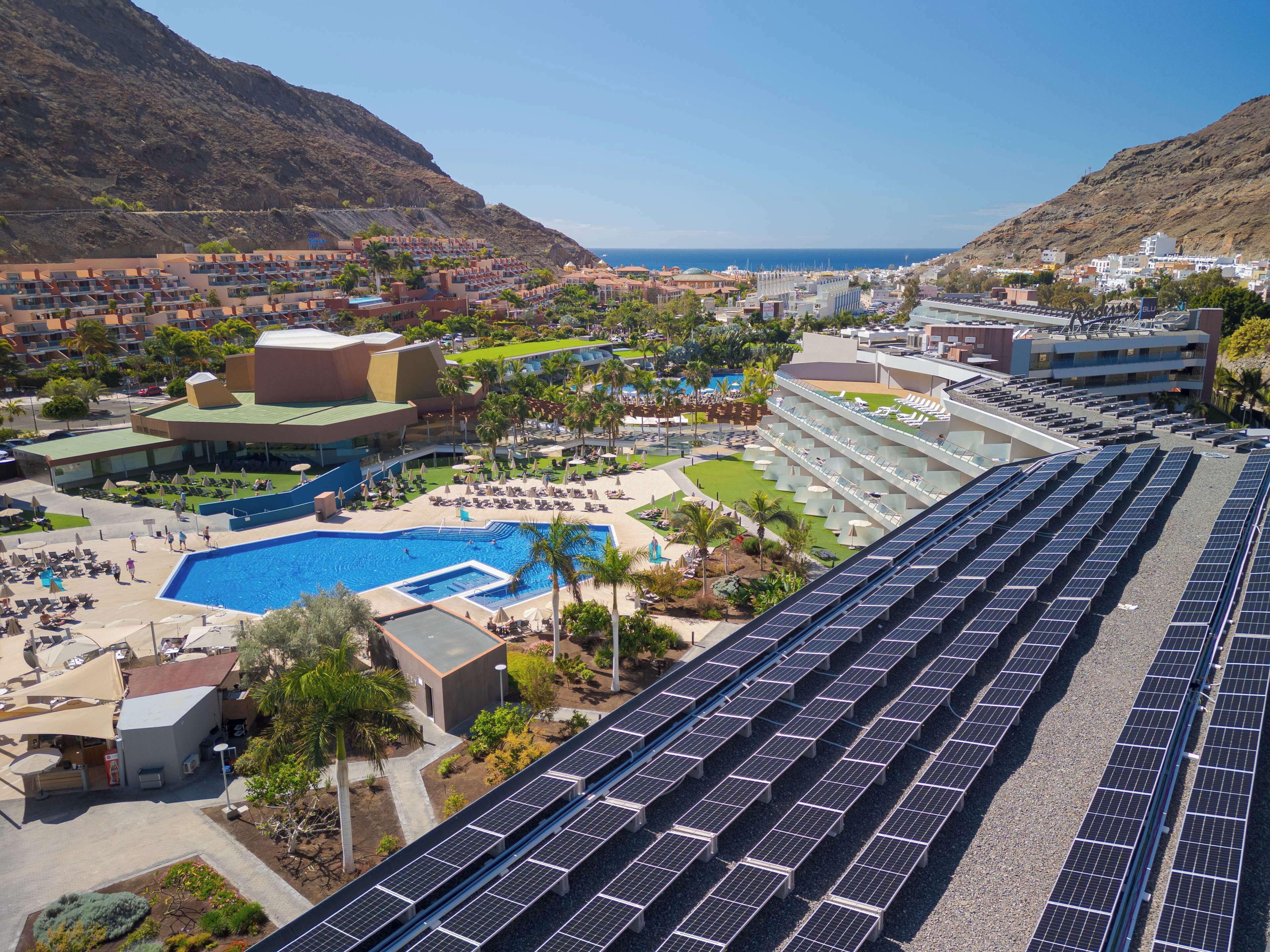 A resort with a large swimming pool, solar panels, and a view of the ocean.