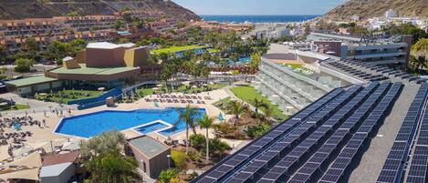 A resort with a large swimming pool, solar panels, and a view of the ocean.