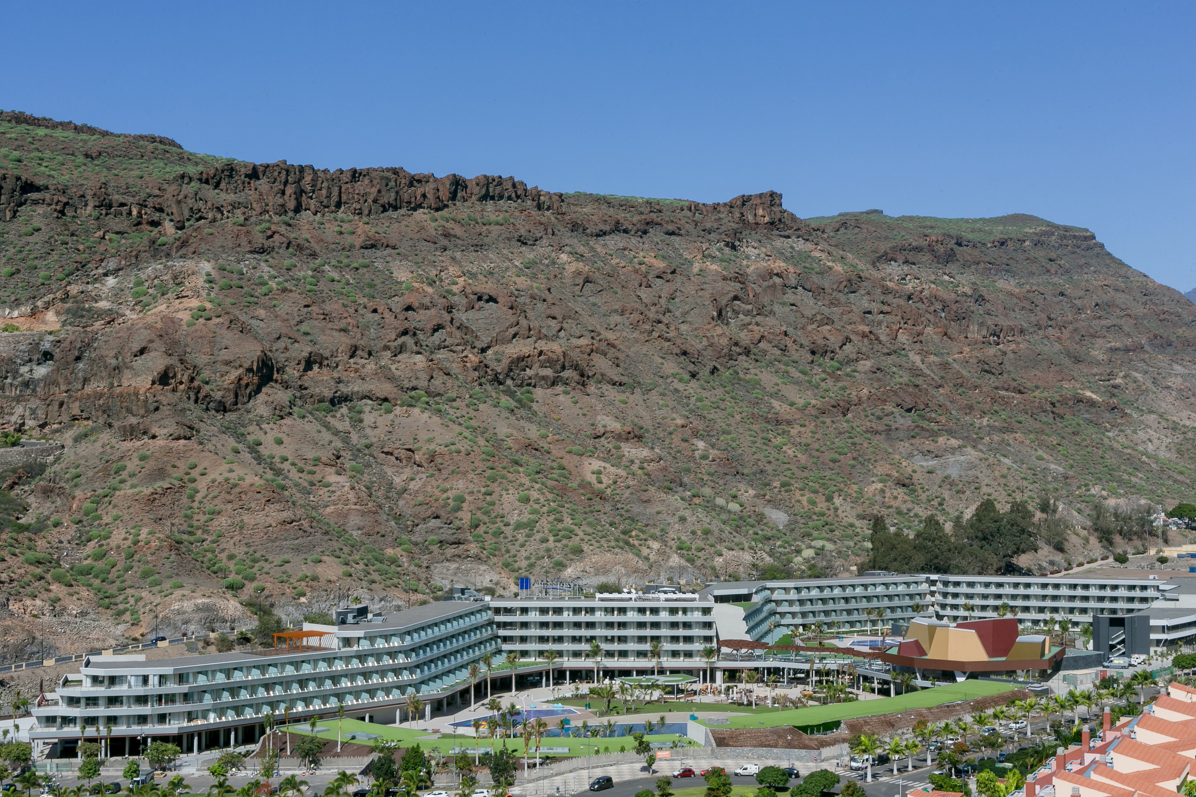 A hotel with multiple floors, a swimming pool, and a view of a rocky hillside.