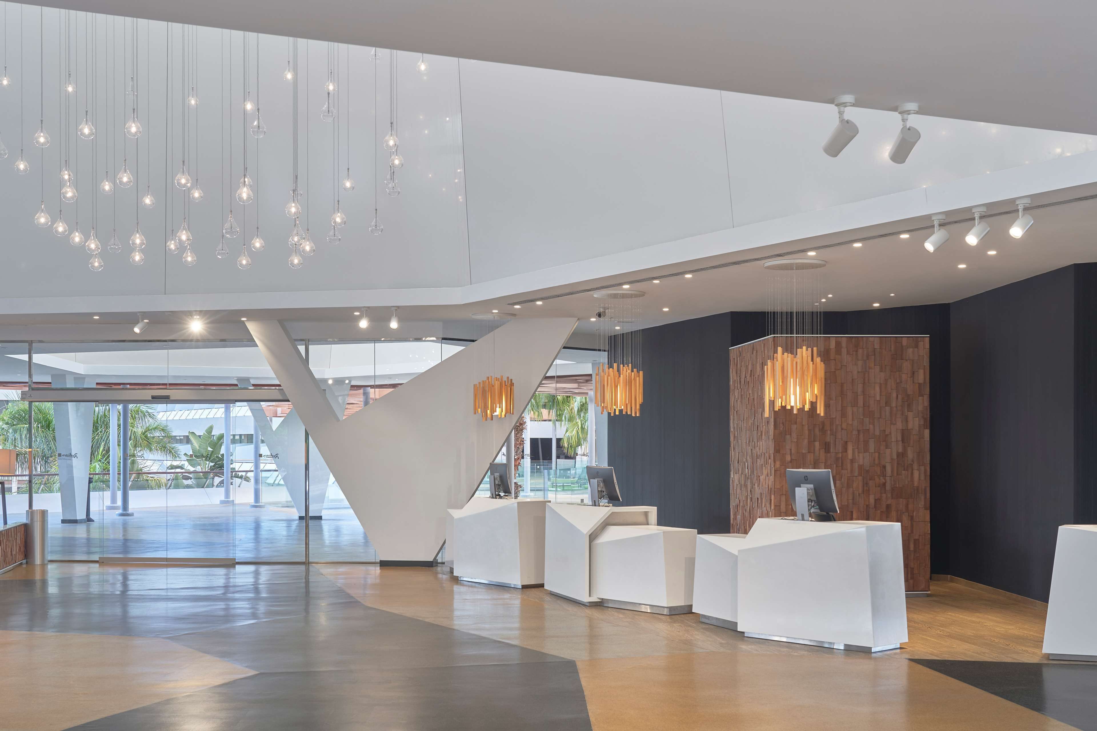 A modern reception area with a central staircase, multiple reception desks, and hanging pendant lights.