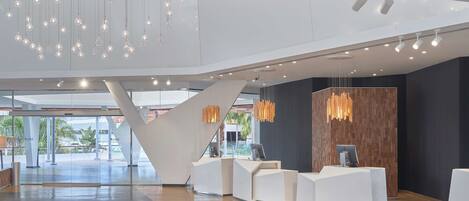 A modern reception area with a central staircase, multiple reception desks, and hanging pendant lights.