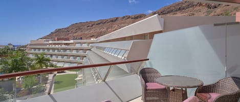 A balcony with wicker furniture and a view of a resort building and mountains.