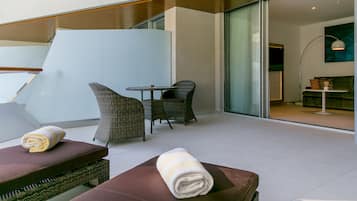 Una habitación moderna con separador de vidrio, una mesita, sillas de mimbre y un sofá con toallas.
