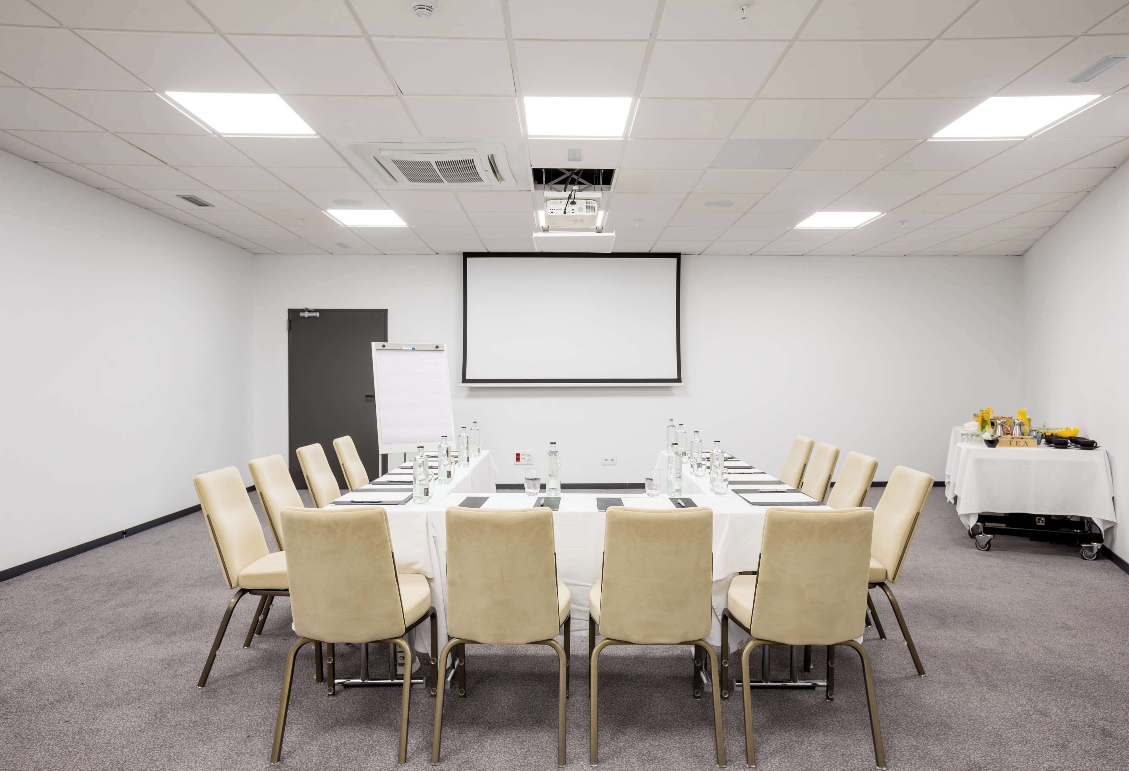 A conference room with a long table, beige chairs, a projector screen, and a whiteboard.