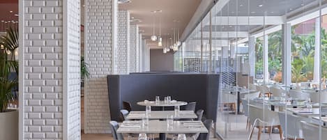 Un comedor moderno con paredes de ladrillo blanco, mesas redondas y separaciones de vidrio.