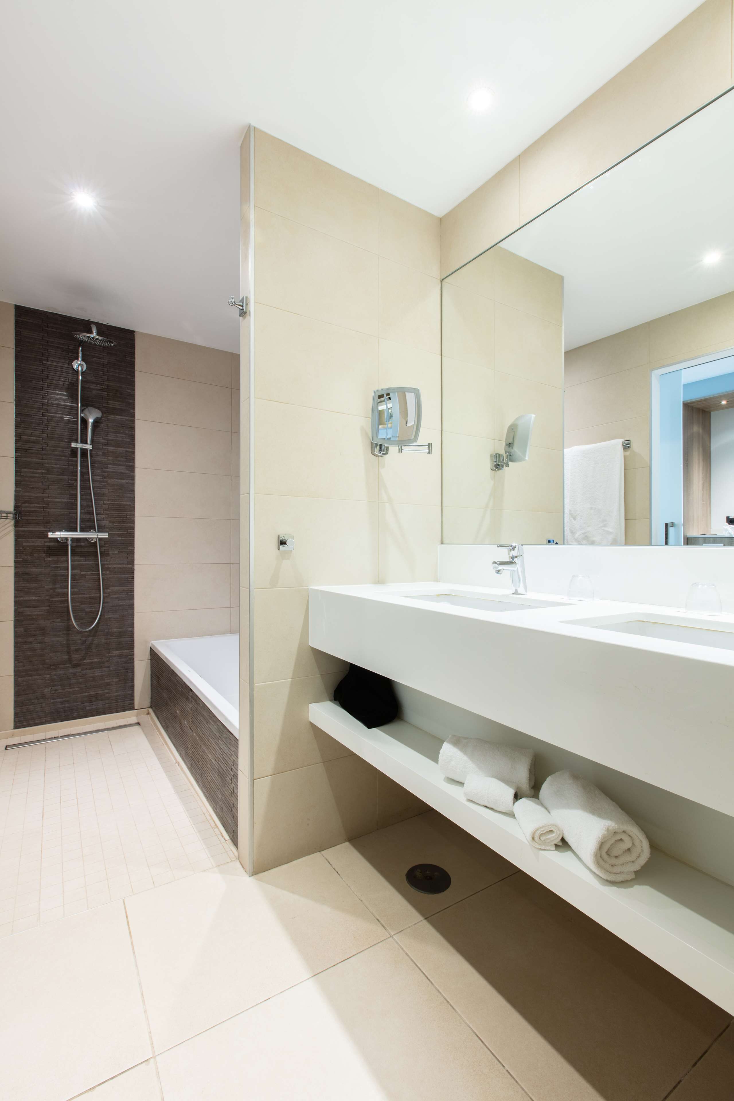 A modern bathroom with a shower, a bathtub, a large mirror, and a vanity with towels.