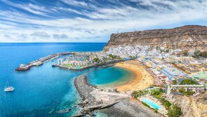 Un pueblo costero con un puerto deportivo, una playa de arena y acantilados rocosos.