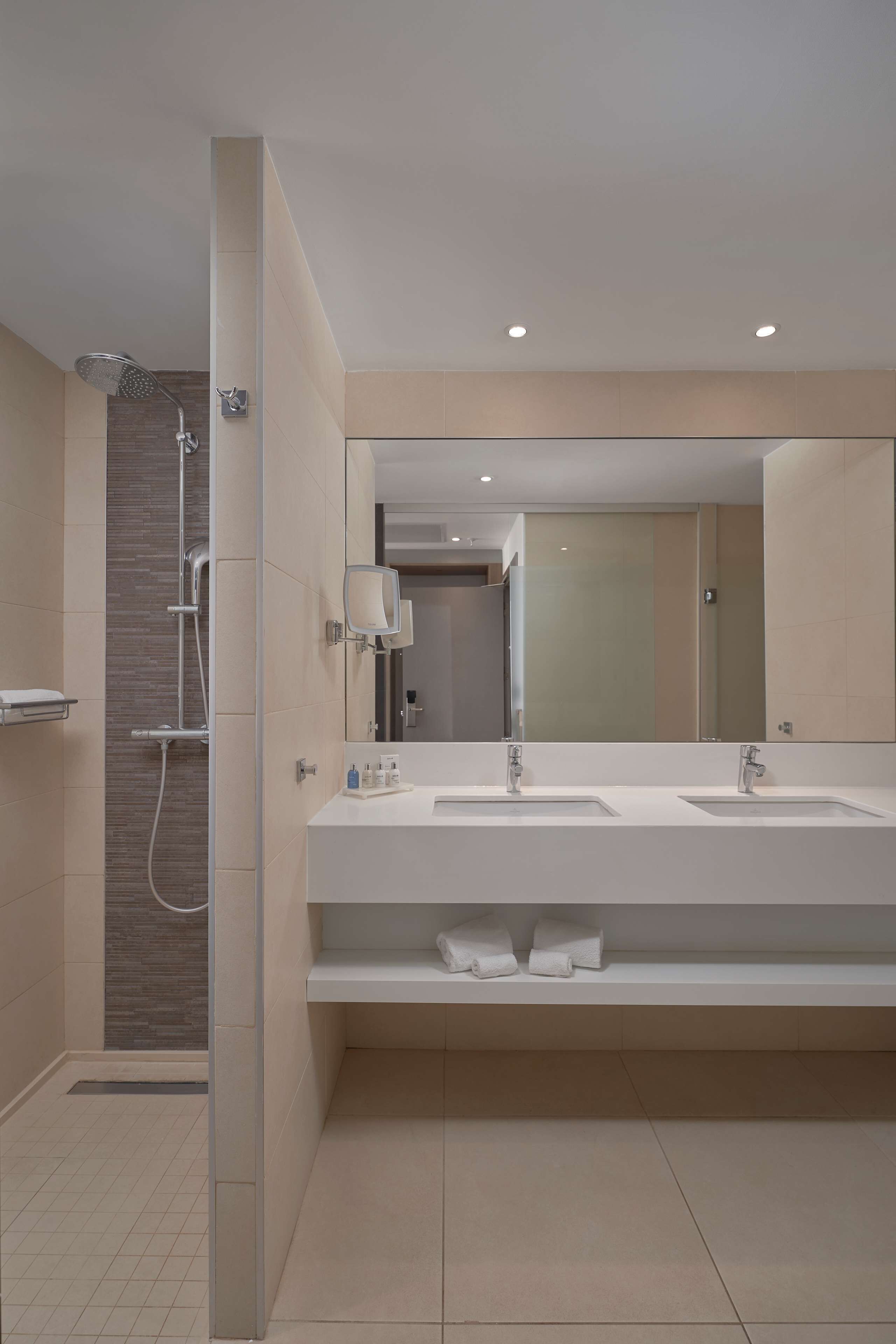 A modern bathroom with two sinks, a large mirror, and a shower area.
