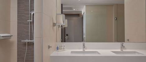 A modern bathroom with two sinks, a large mirror, and a shower area.