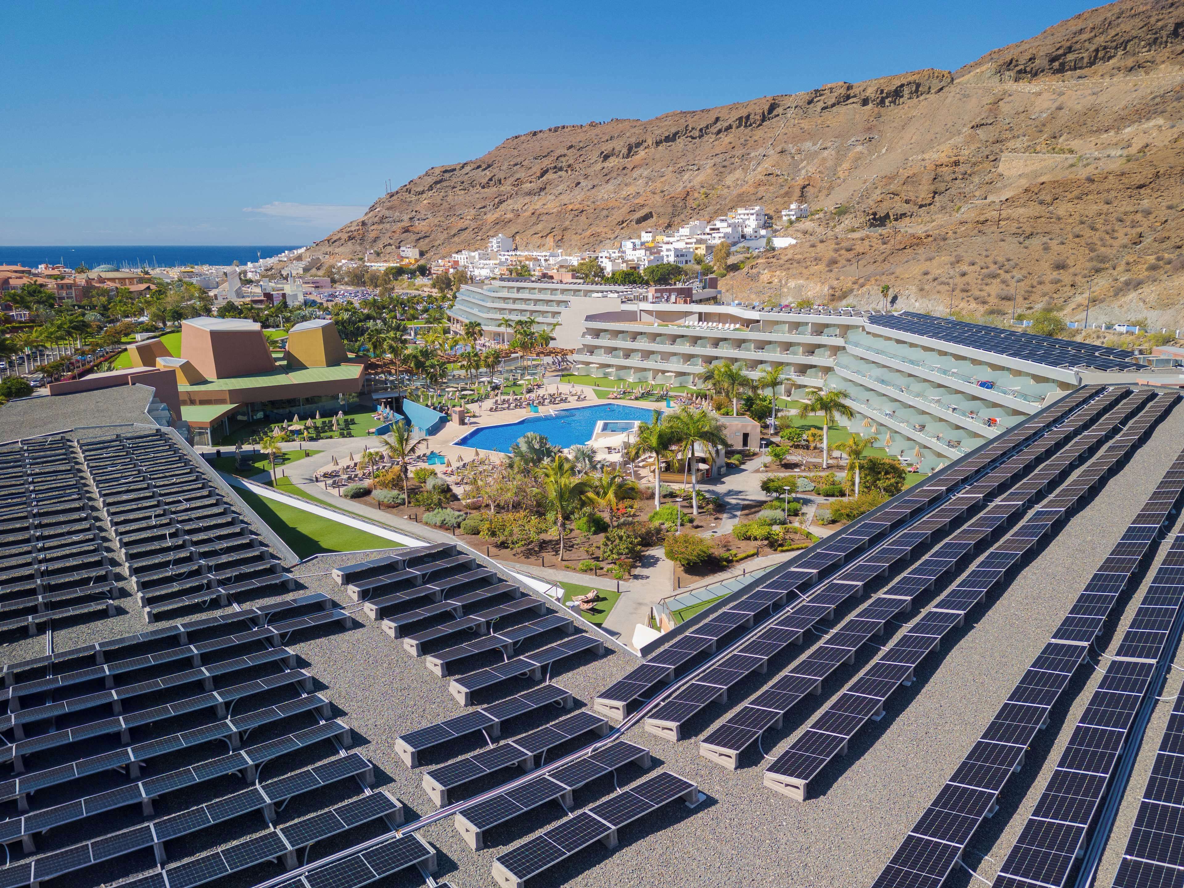 A resort with a large pool, solar panels, and a mountainous backdrop.