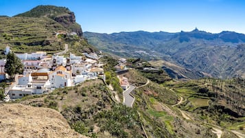 A coastal village with white buildings, terraced fields, and a mountain backdrop.