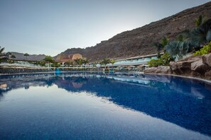 Une piscine à l’eau cristalline, entourée de chaises longues et de parasols, avec une montagne en toile de fond.