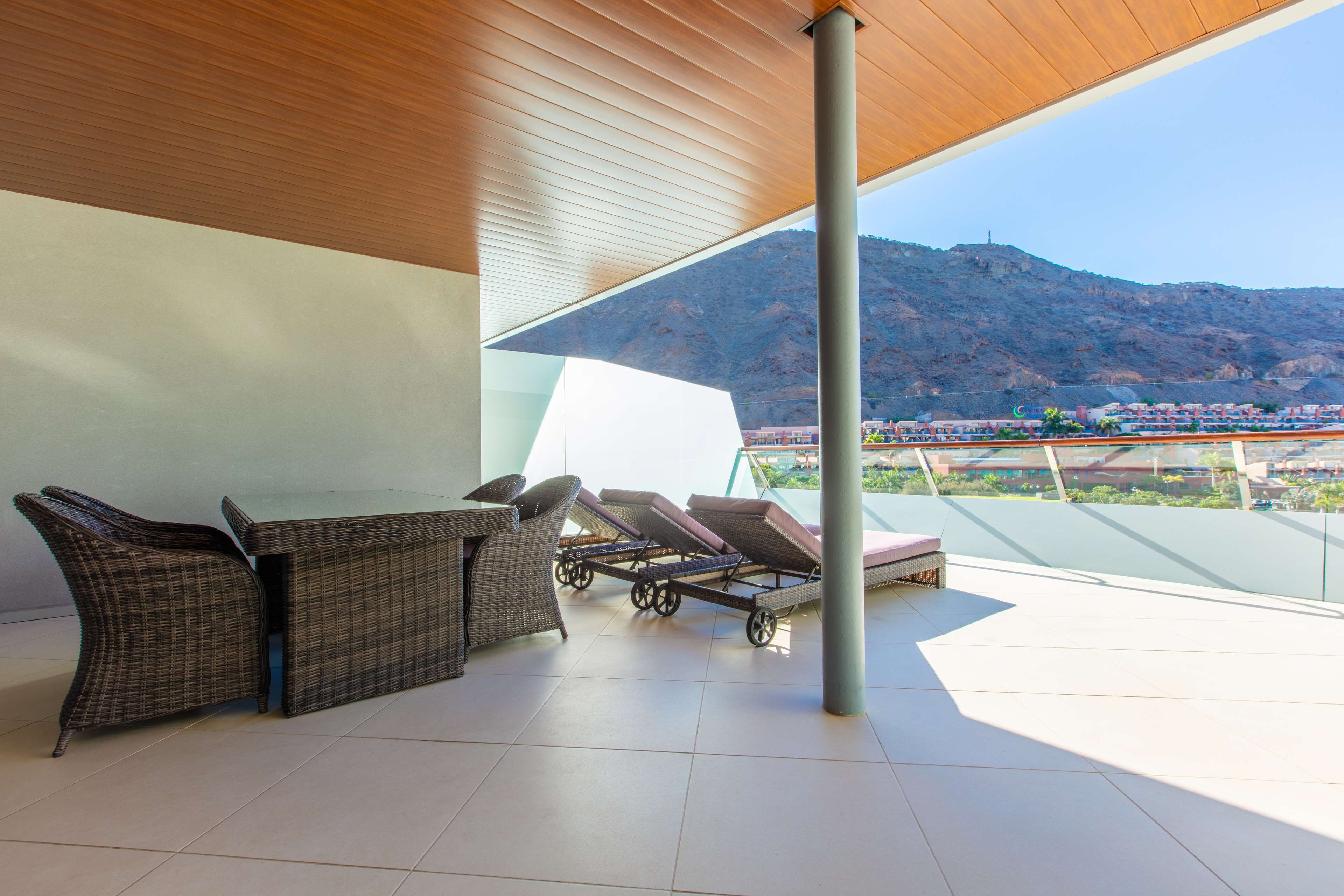 A covered outdoor seating area with wicker furniture and a view of a mountainous landscape.