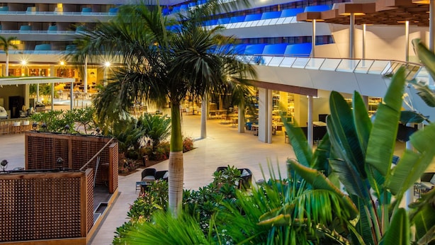 Un hotel moderno con varios pisos, zonas de estar al aire libre y abundante vegetación.