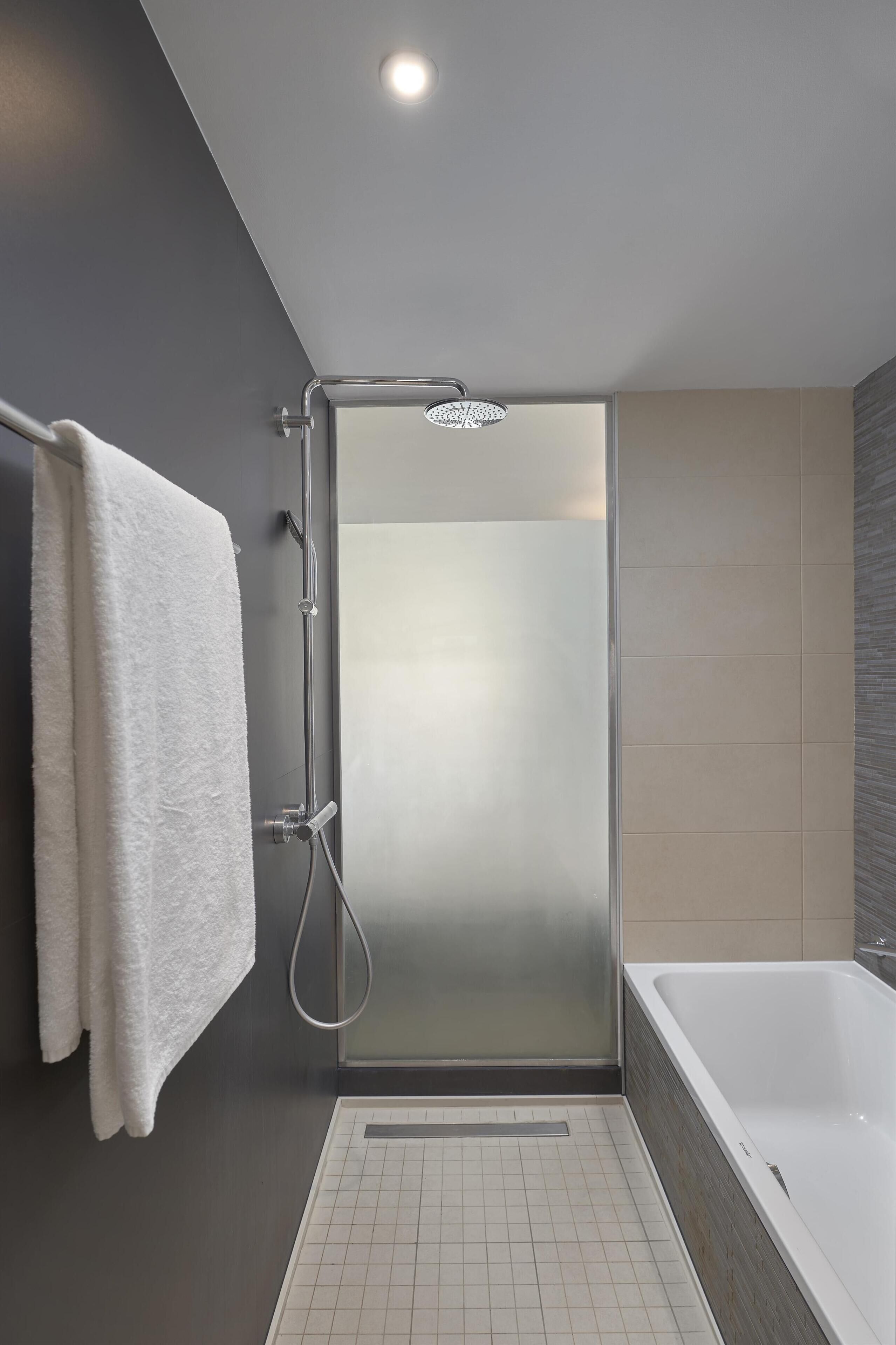A modern bathroom with a glass-enclosed shower, a white bathtub, and a towel hanging on a rack.