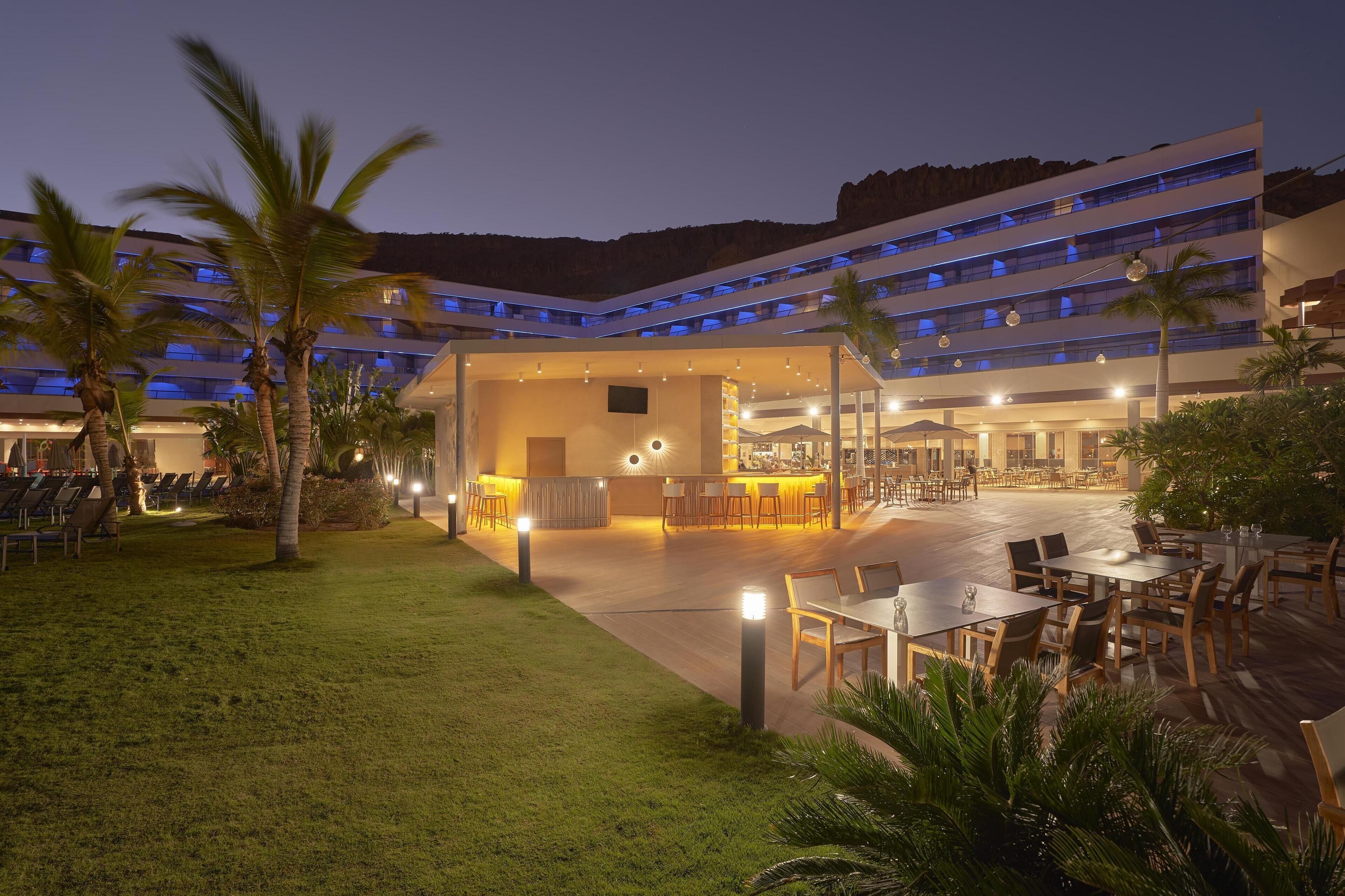 Un hotel con un amplio espacio exterior, varias mesas de comedor y una zona de bar/lounge.