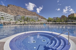 A hotel pool with a hot tub, palm trees, and a mountainous backdrop.