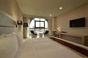 Habitación de hotel con una cama grande, un televisor montado en la pared, un escritorio con una silla y vistas a través de un ventanal amplio.