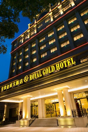 Un hotel con un cartel llamativo que dice 'ROYAL GOLD HOTEL' y una entrada imponente con columnas y una escalera.