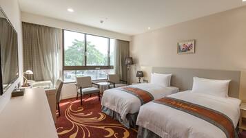 A hotel room with two beds, a desk, a chair, a window with curtains, a lamp, and a painting on the wall.