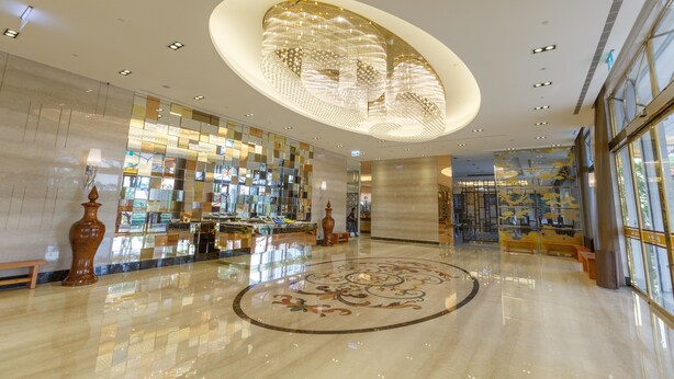 A spacious lobby with a polished floor, a central decorative light fixture, and a large glass wall with reflections. - Royal Gold Hotel (Kaohsiung)