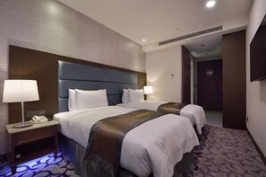 Habitación de hotel con dos camas, una mesita de noche, una lámpara y piso alfombrado.