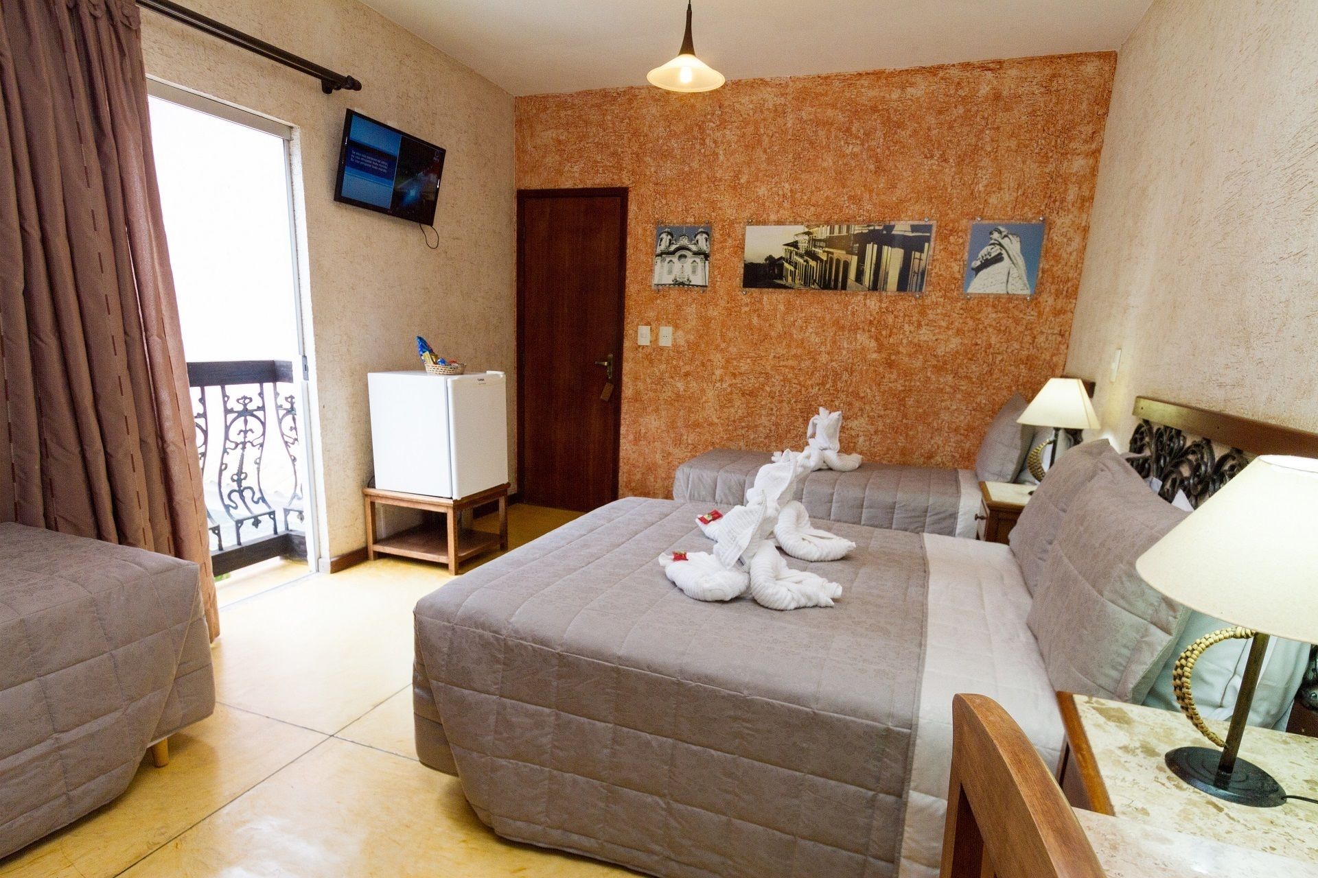 A hotel room with a bed, a small desk, a television, and a wall with pictures.