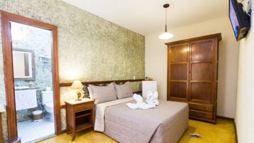 A bedroom with a bed, a wooden wardrobe, a nightstand with a lamp, and a television mounted on the wall.