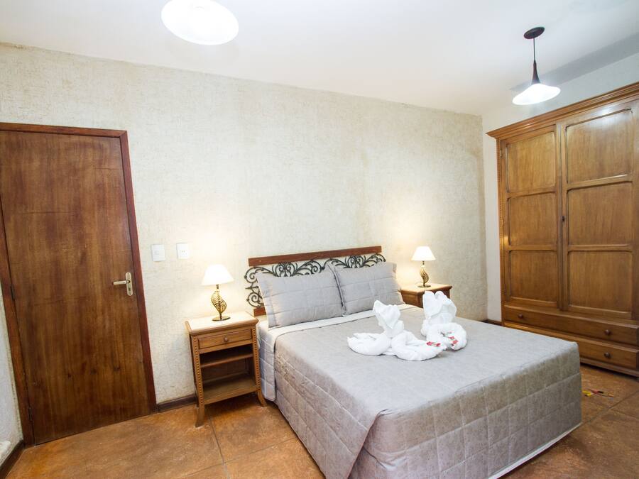 A bedroom with a bed, two bedside tables with lamps, a wardrobe, and a door.
